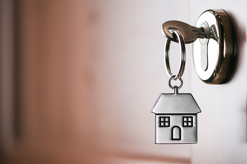 House key on a house shaped silver keyring in the lock of a entrance brown door